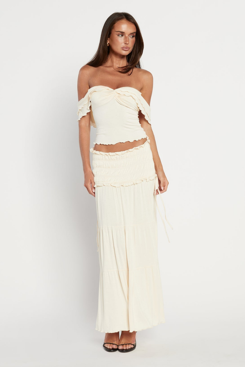 Woman in cream ribbed knit off-the-shoulder top and tiered maxi skirt