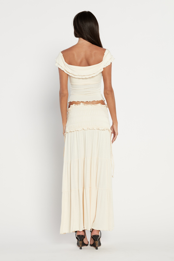Woman in cream ribbed knit off-the-shoulder top and tiered maxi skirt