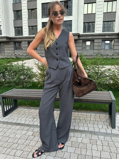 Woman in gray wool blend vest and wide leg pants holding a coffee cup and design book.