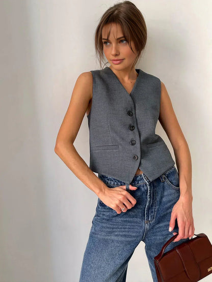 Woman in gray wool blend vest and wide leg pants holding a coffee cup and design book.