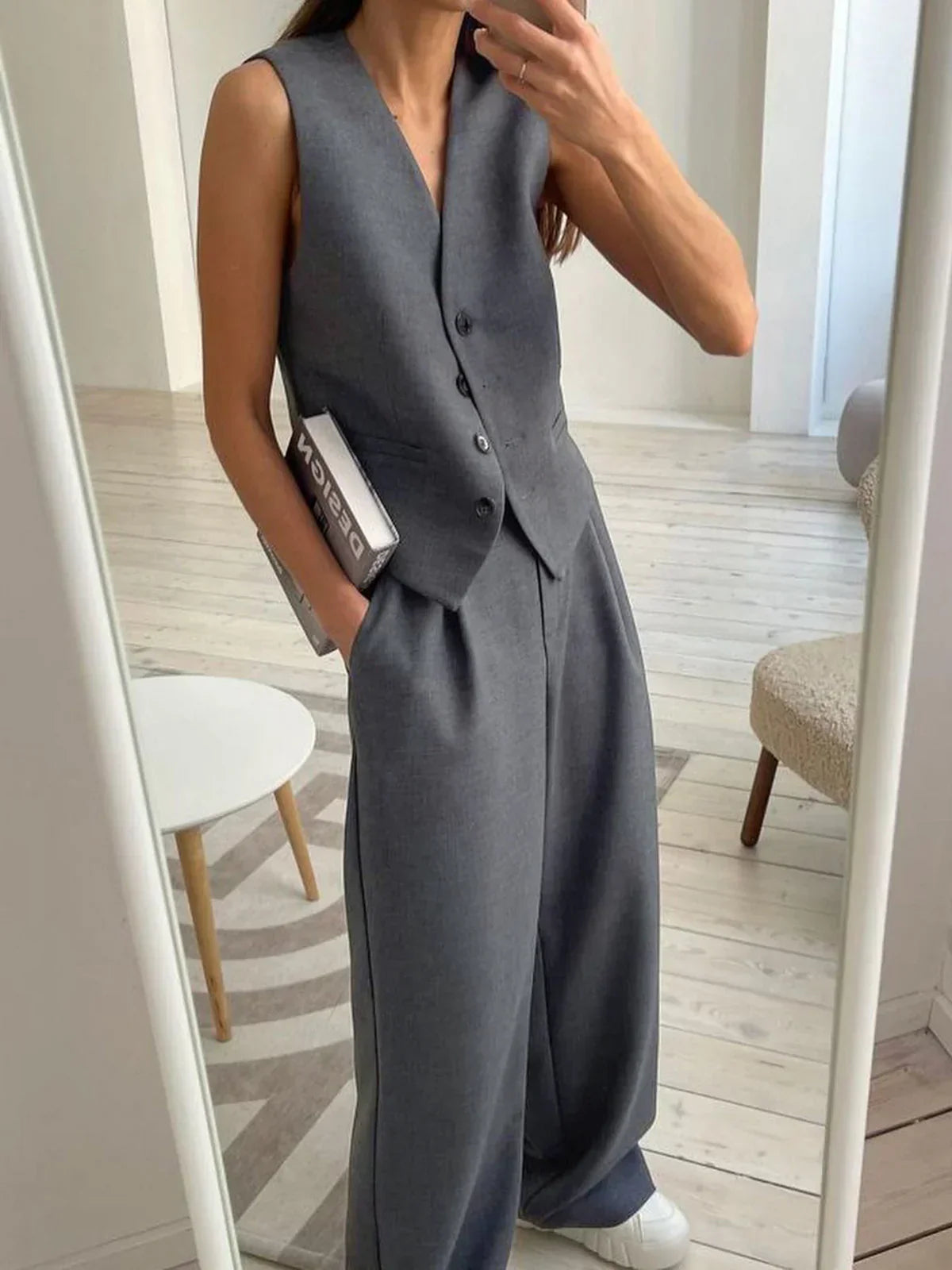Woman in gray wool blend vest and wide leg pants holding a coffee cup and design book.