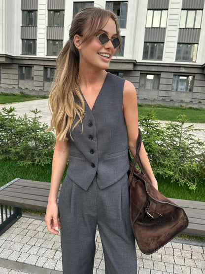 Woman in gray wool blend vest and wide leg pants holding a coffee cup and design book.