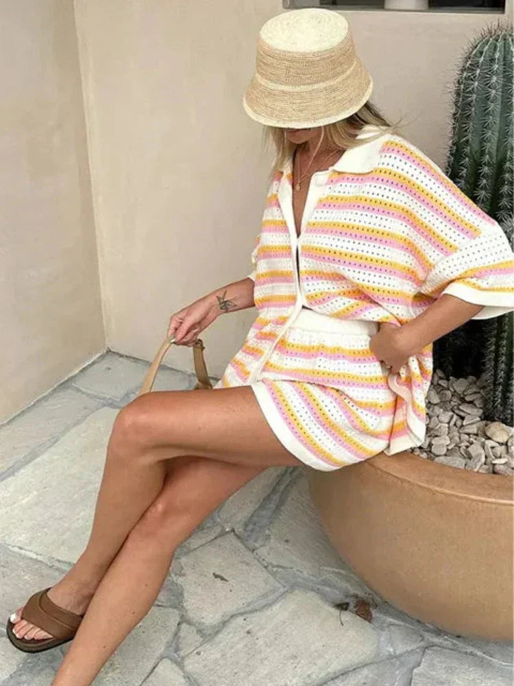 Woman in pink and yellow striped knit cardigan and shorts set sitting by pool.
