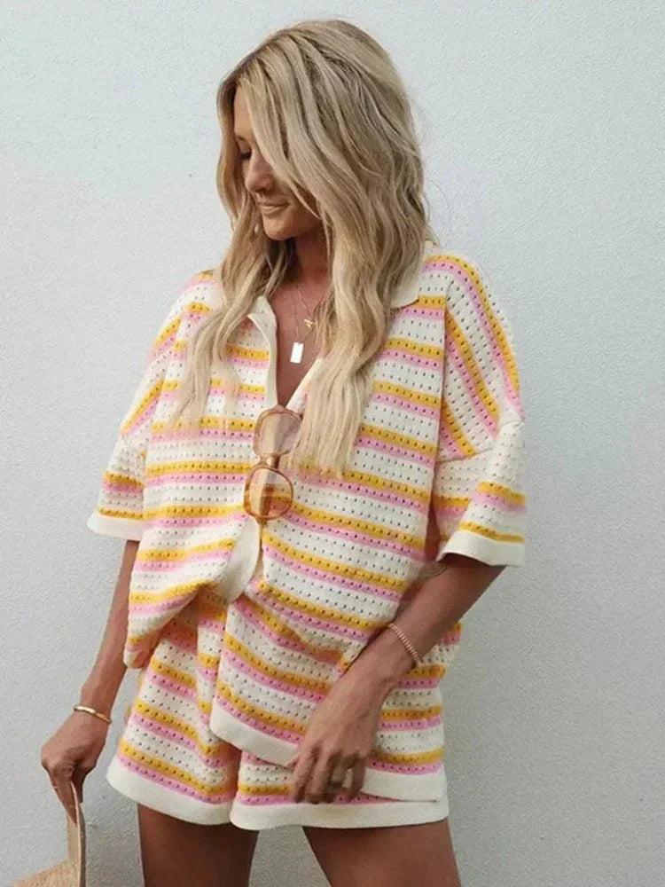 Woman in pink and yellow striped knit cardigan and shorts set sitting by pool.
