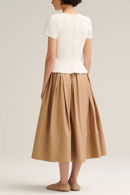 Woman wearing off-white pleated maxi skirt set with peplum top and white heels