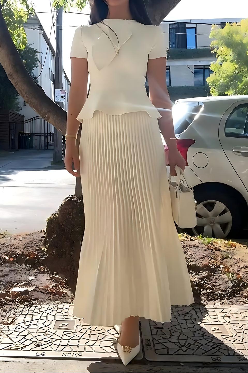 Woman wearing off-white pleated maxi skirt set with peplum top and white heels
