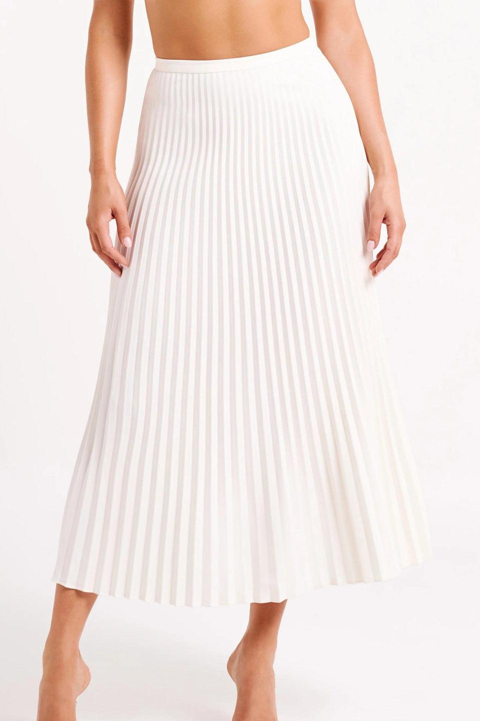 Woman wearing off-white pleated maxi skirt set with peplum top and white heels