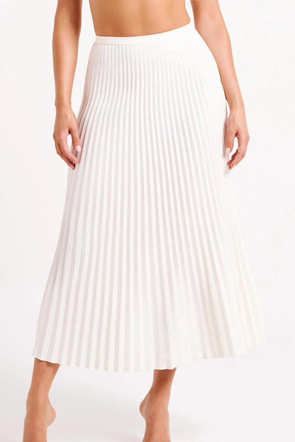 Woman wearing off-white pleated maxi skirt set with peplum top and white heels