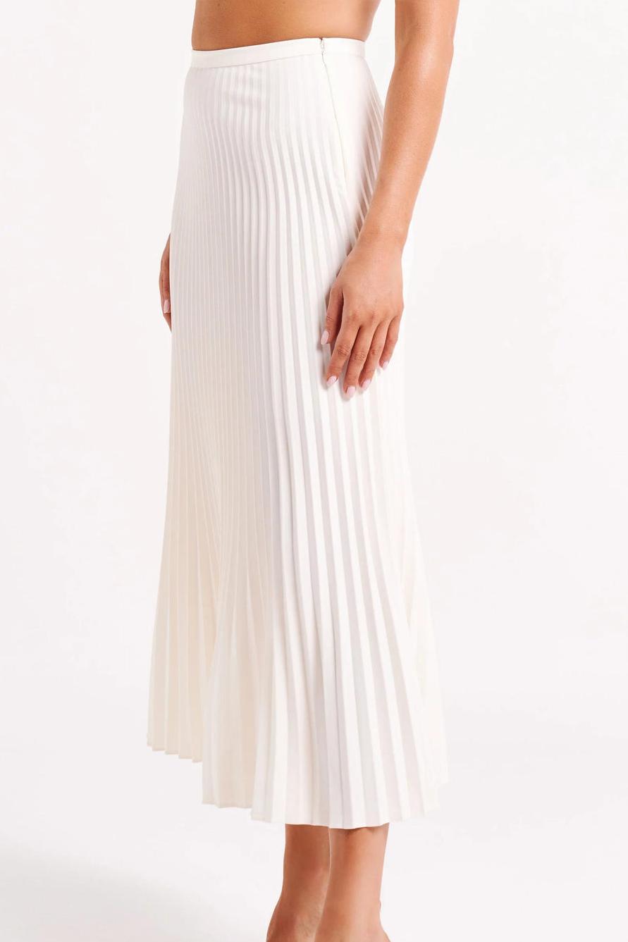 Woman wearing off-white pleated maxi skirt set with peplum top and white heels