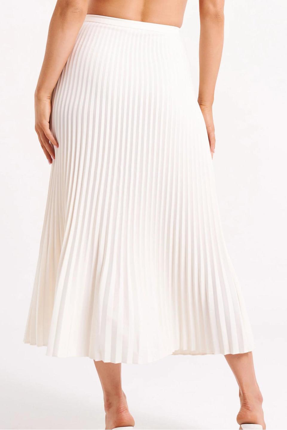 Woman wearing off-white pleated maxi skirt set with peplum top and white heels