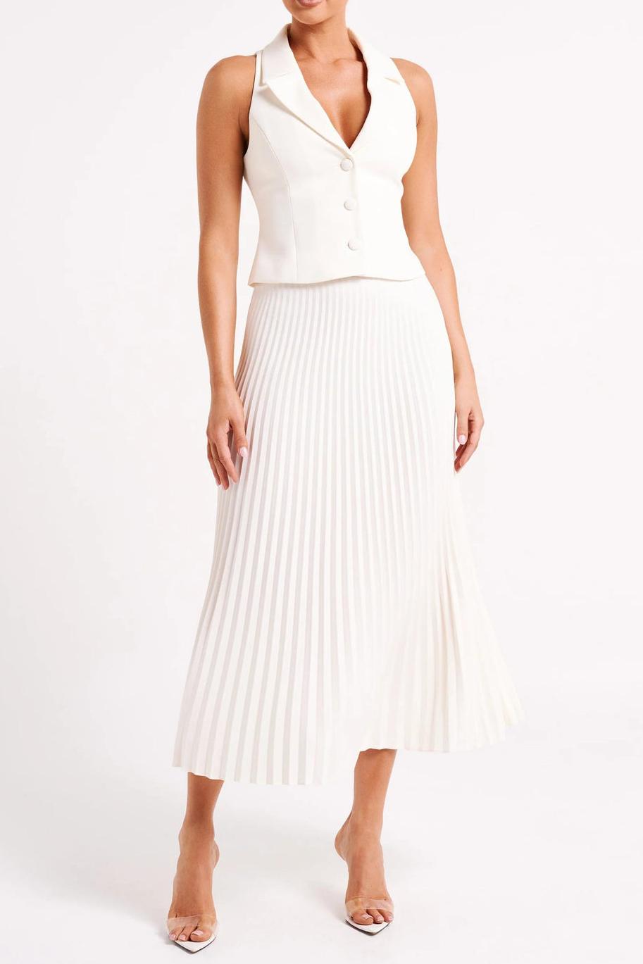 Woman wearing off-white pleated maxi skirt set with peplum top and white heels