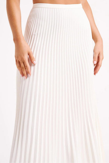 Woman wearing off-white pleated maxi skirt set with peplum top and white heels
