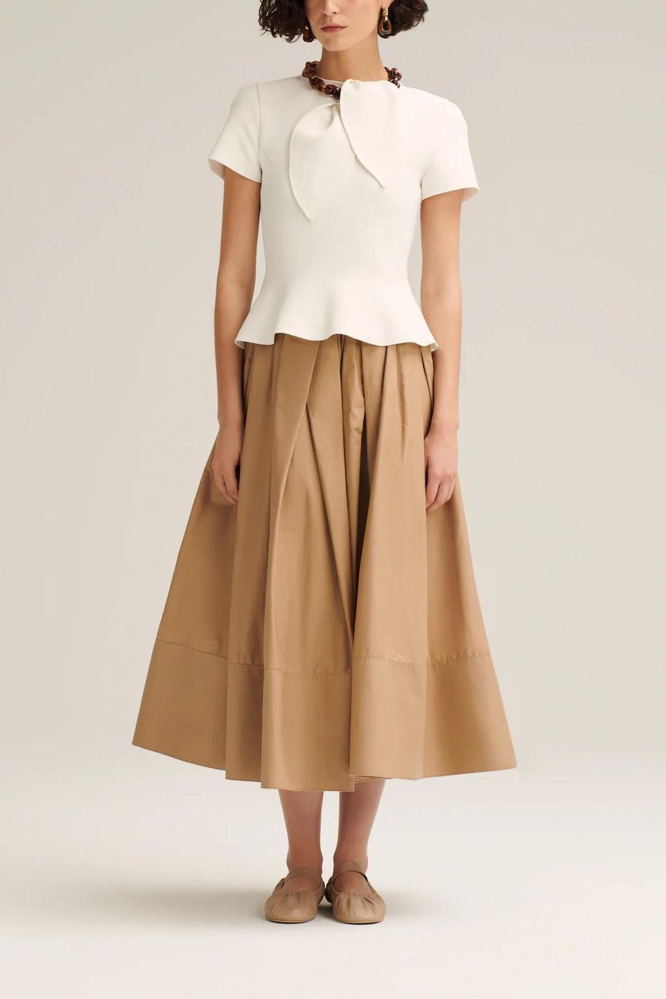 Woman wearing off-white pleated maxi skirt set with peplum top and white heels