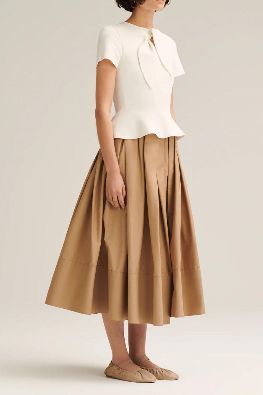 Woman wearing off-white pleated maxi skirt set with peplum top and white heels