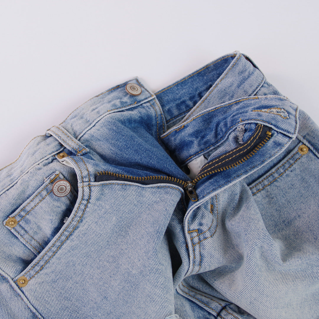 Woman wearing light wash denim shorts with asymmetrical waist and distressed hem.