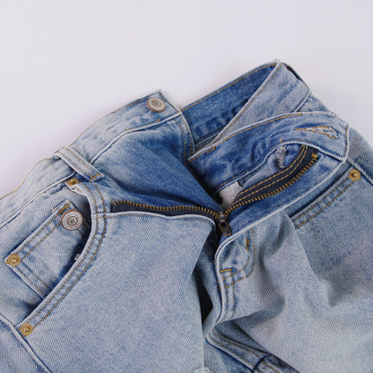 Woman wearing light wash denim shorts with asymmetrical waist and distressed hem.