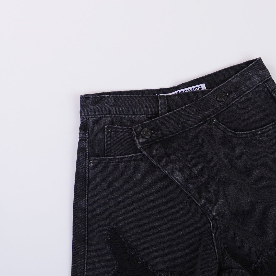 Woman wearing light wash denim shorts with asymmetrical waist and distressed hem.