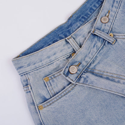 Woman wearing light wash denim shorts with asymmetrical waist and distressed hem.