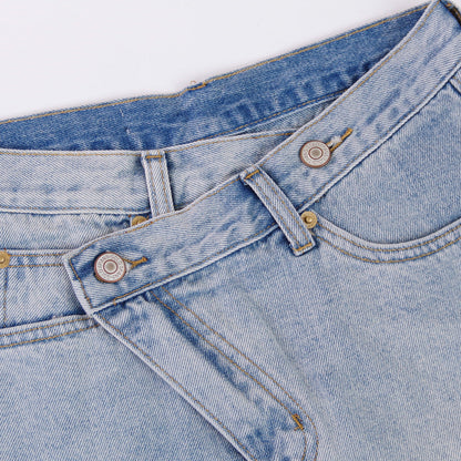 Woman wearing light wash denim shorts with asymmetrical waist and distressed hem.