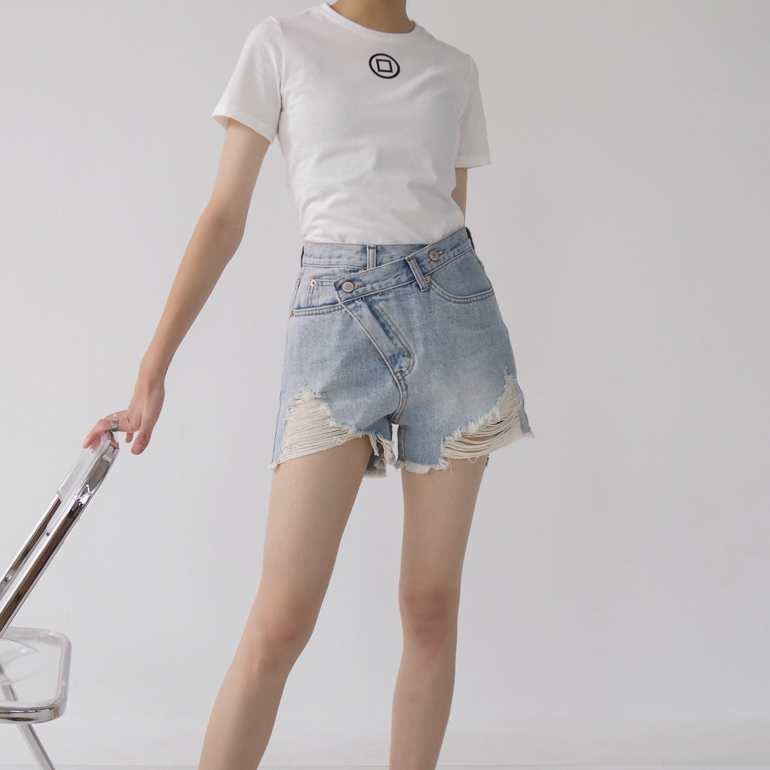 Woman wearing light wash denim shorts with asymmetrical waist and distressed hem.