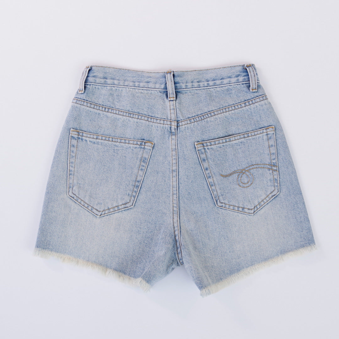 Woman wearing light wash denim shorts with asymmetrical waist and distressed hem.