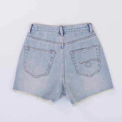 Woman wearing light wash denim shorts with asymmetrical waist and distressed hem.