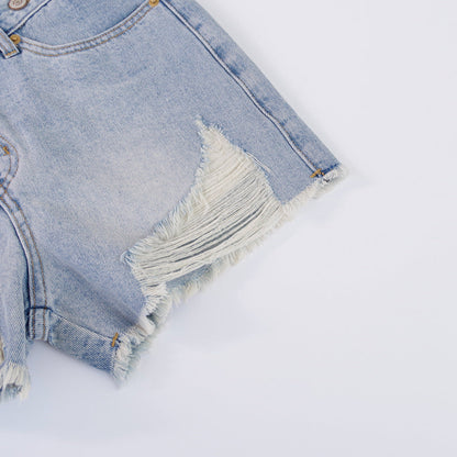 Woman wearing light wash denim shorts with asymmetrical waist and distressed hem.