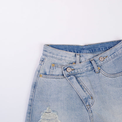 Woman wearing light wash denim shorts with asymmetrical waist and distressed hem.