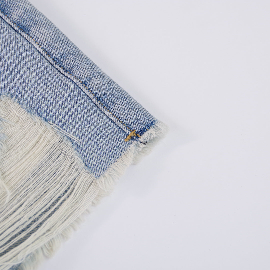 Woman wearing light wash denim shorts with asymmetrical waist and distressed hem.