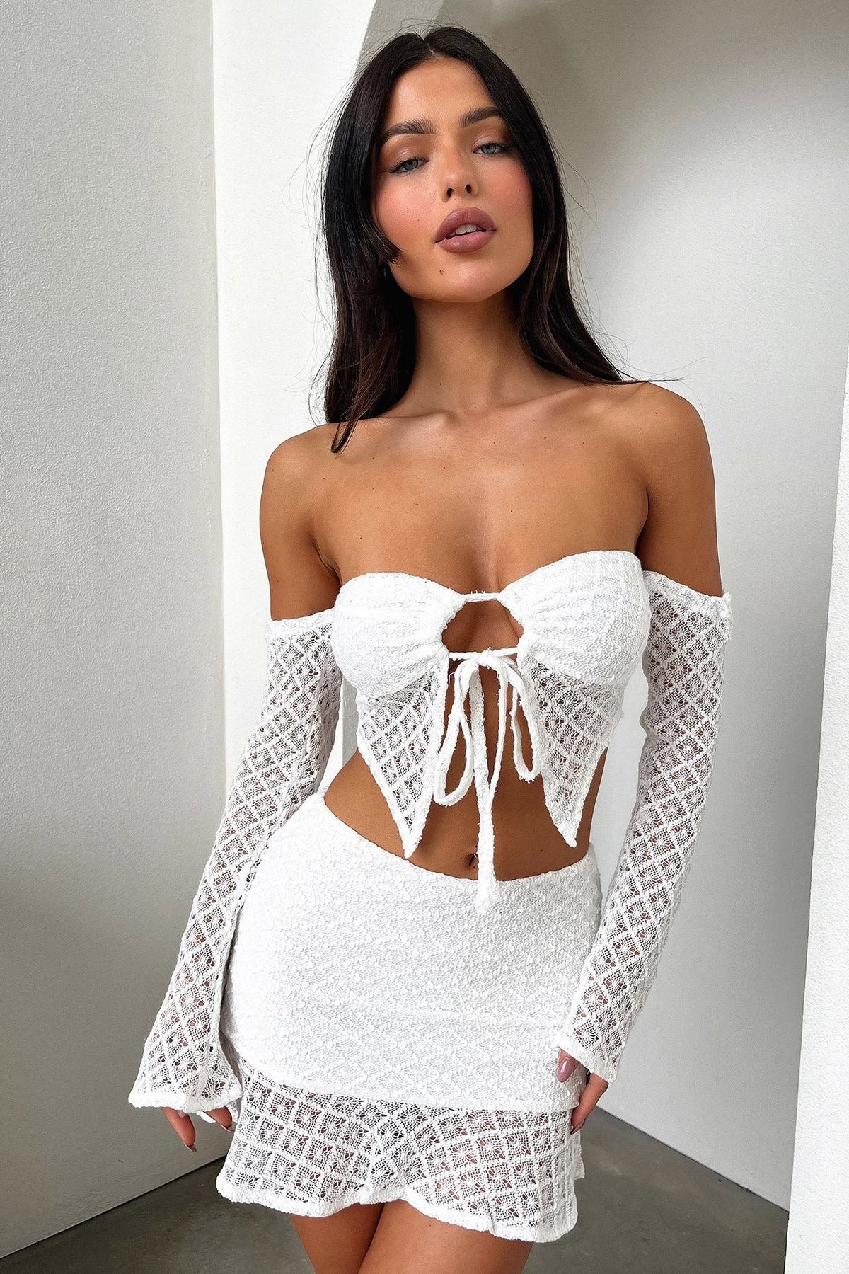 Woman in white crochet knit two-piece set, featuring a tie-front top and mini skirt.