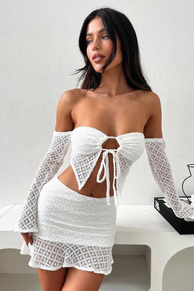 Woman in white crochet knit two-piece set, featuring a tie-front top and mini skirt.