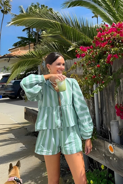 Woman in striped green cotton shorts set holding a drink.