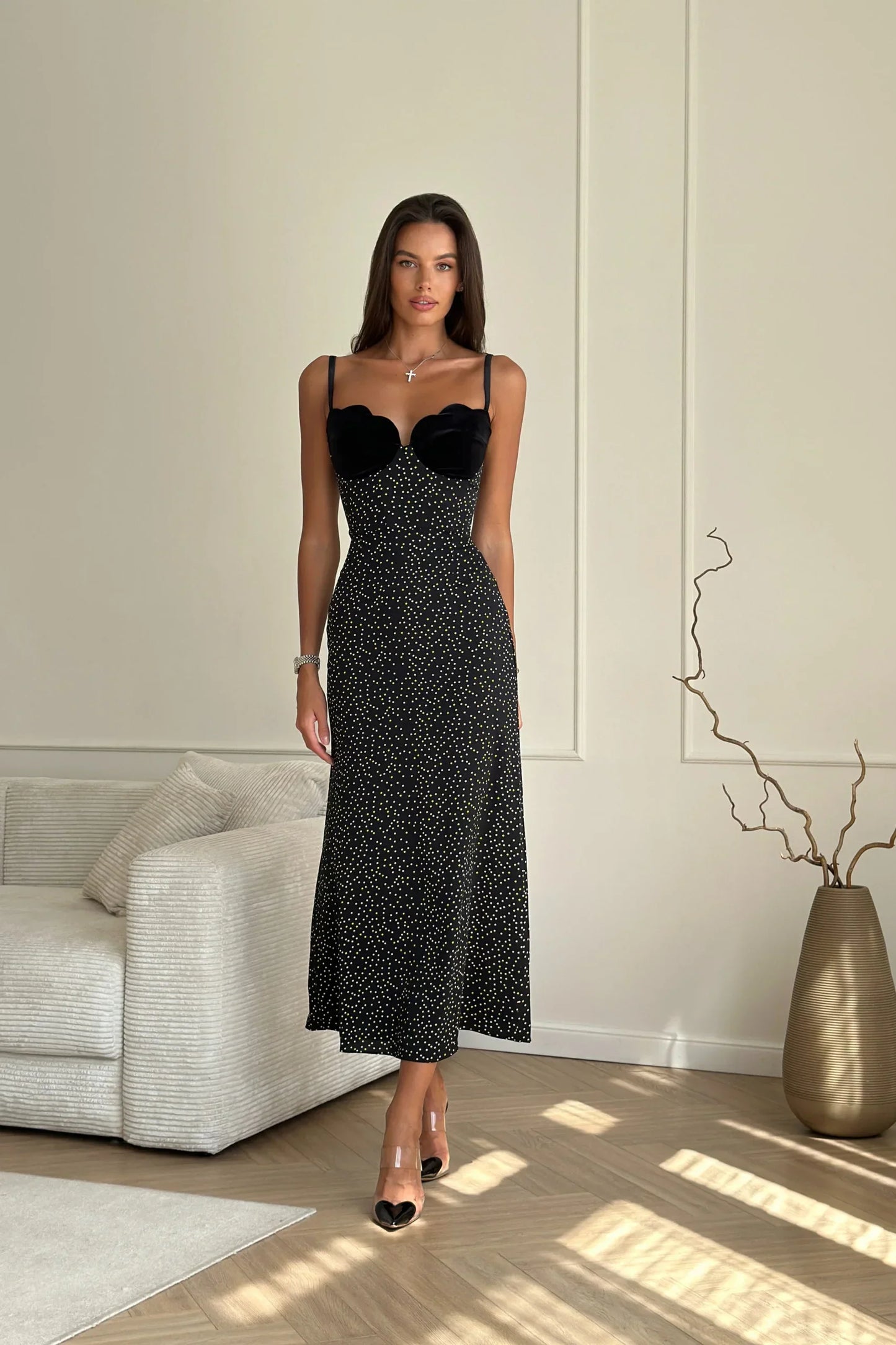 Woman in black polka dot midi dress with velvet bodice leaning against white wall