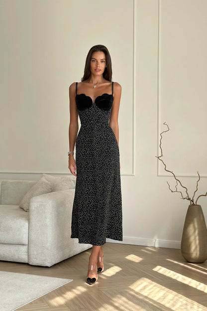 Woman in black polka dot midi dress with velvet bodice leaning against white wall