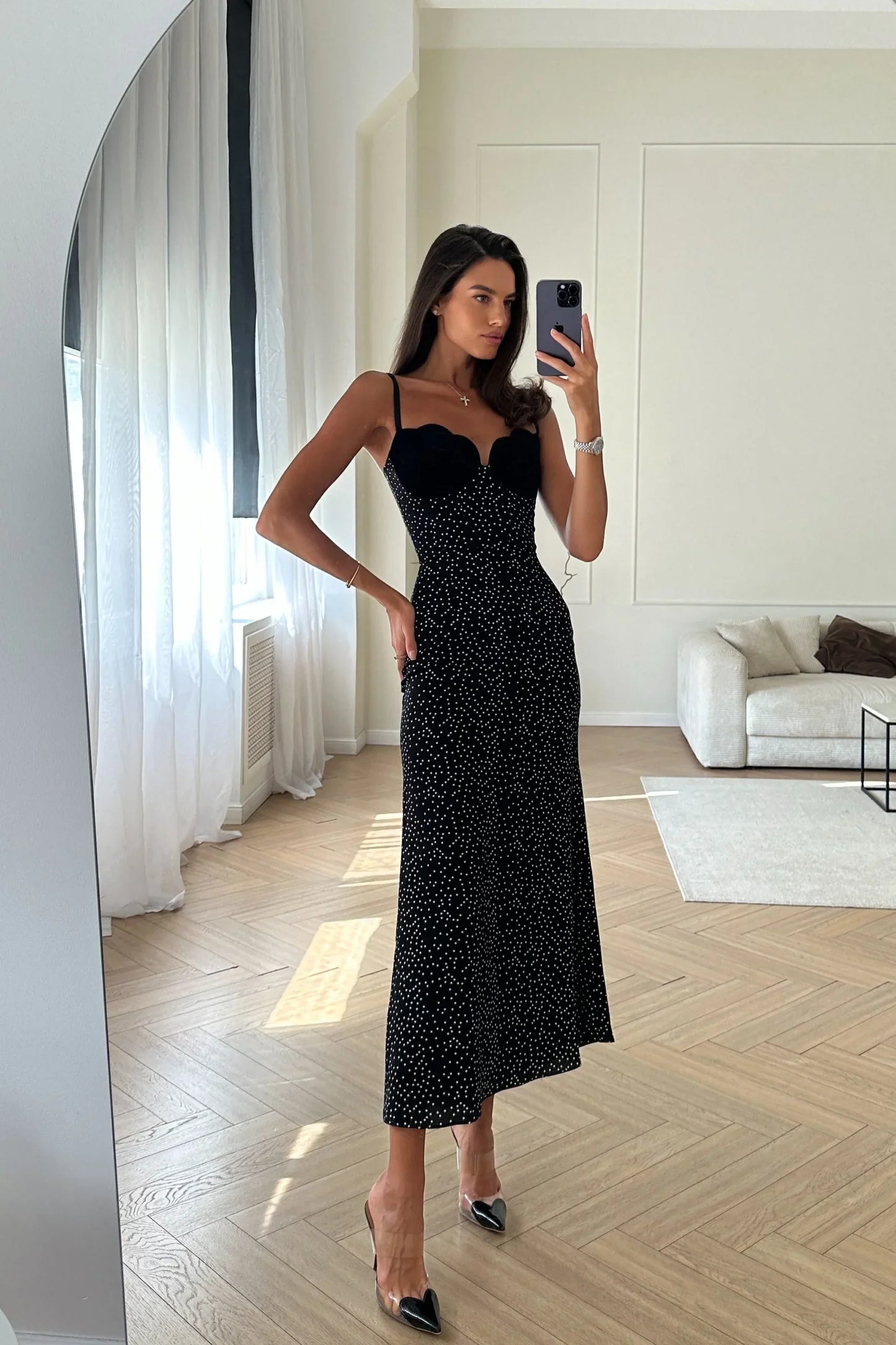 Woman in black polka dot midi dress with velvet bodice leaning against white wall