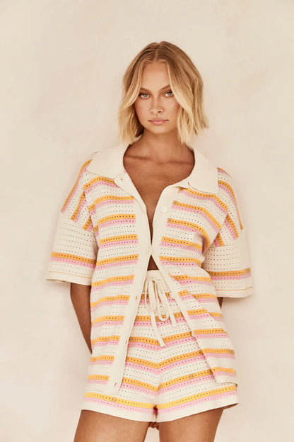 Woman in pink and yellow striped knit cardigan and shorts set sitting by pool.