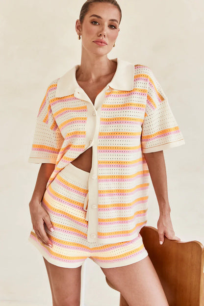 Woman in pink and yellow striped knit cardigan and shorts set sitting by pool.