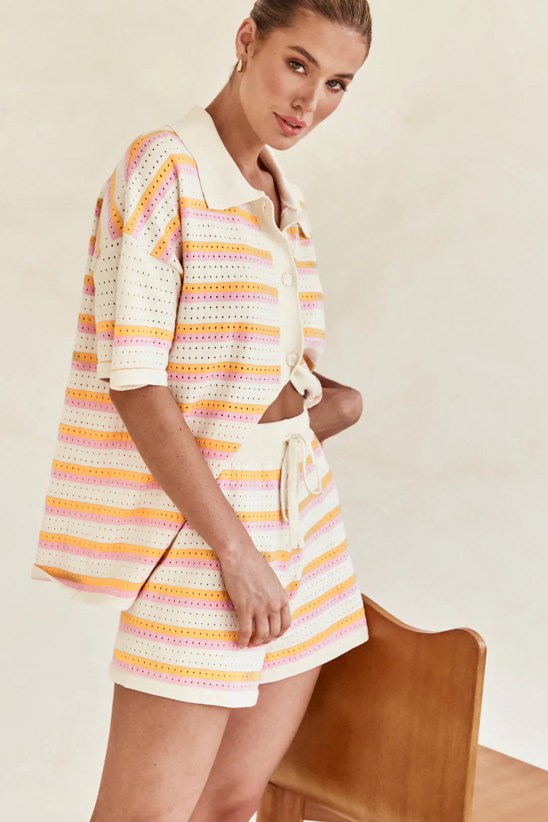 Woman in pink and yellow striped knit cardigan and shorts set sitting by pool.
