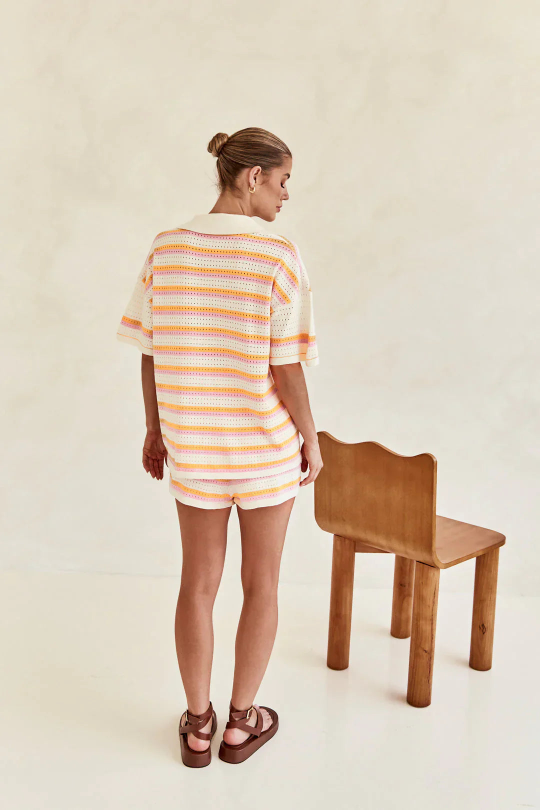 Woman in pink and yellow striped knit cardigan and shorts set sitting by pool.