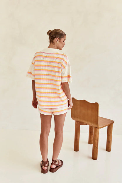 Woman in pink and yellow striped knit cardigan and shorts set sitting by pool.