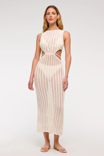 Woman wearing a long, off-white crochet knit dress with waist cutouts.