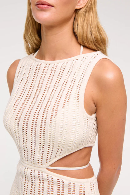 Woman wearing a long, off-white crochet knit dress with waist cutouts.