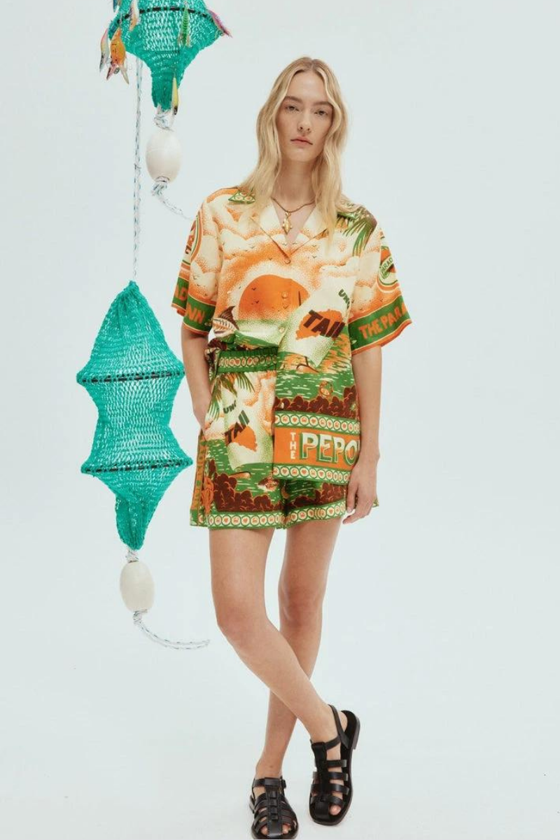 Woman wearing orange and green tropical print short set with black sandals.