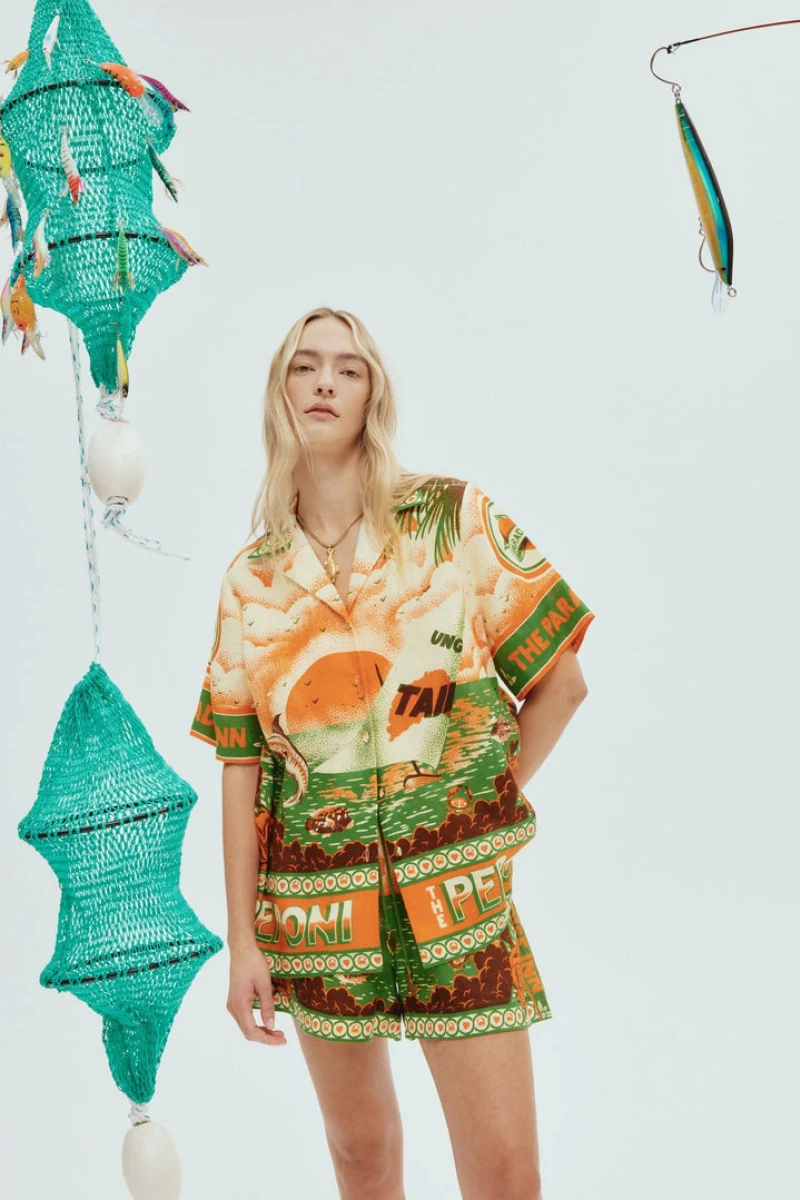 Woman wearing orange and green tropical print short set with black sandals.