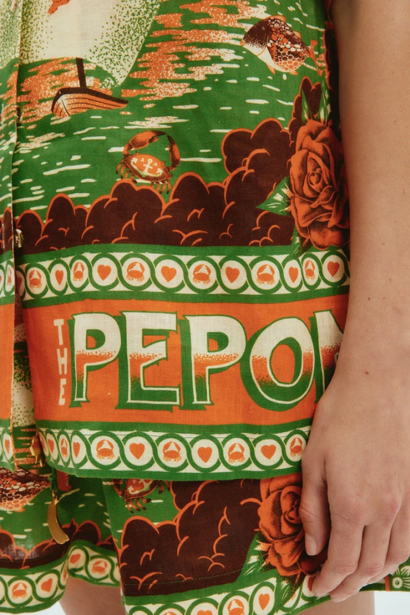 Woman wearing orange and green tropical print short set with black sandals.
