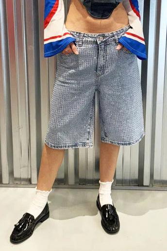 Woman wearing light wash denim bermuda shorts with sparkly embellishments
