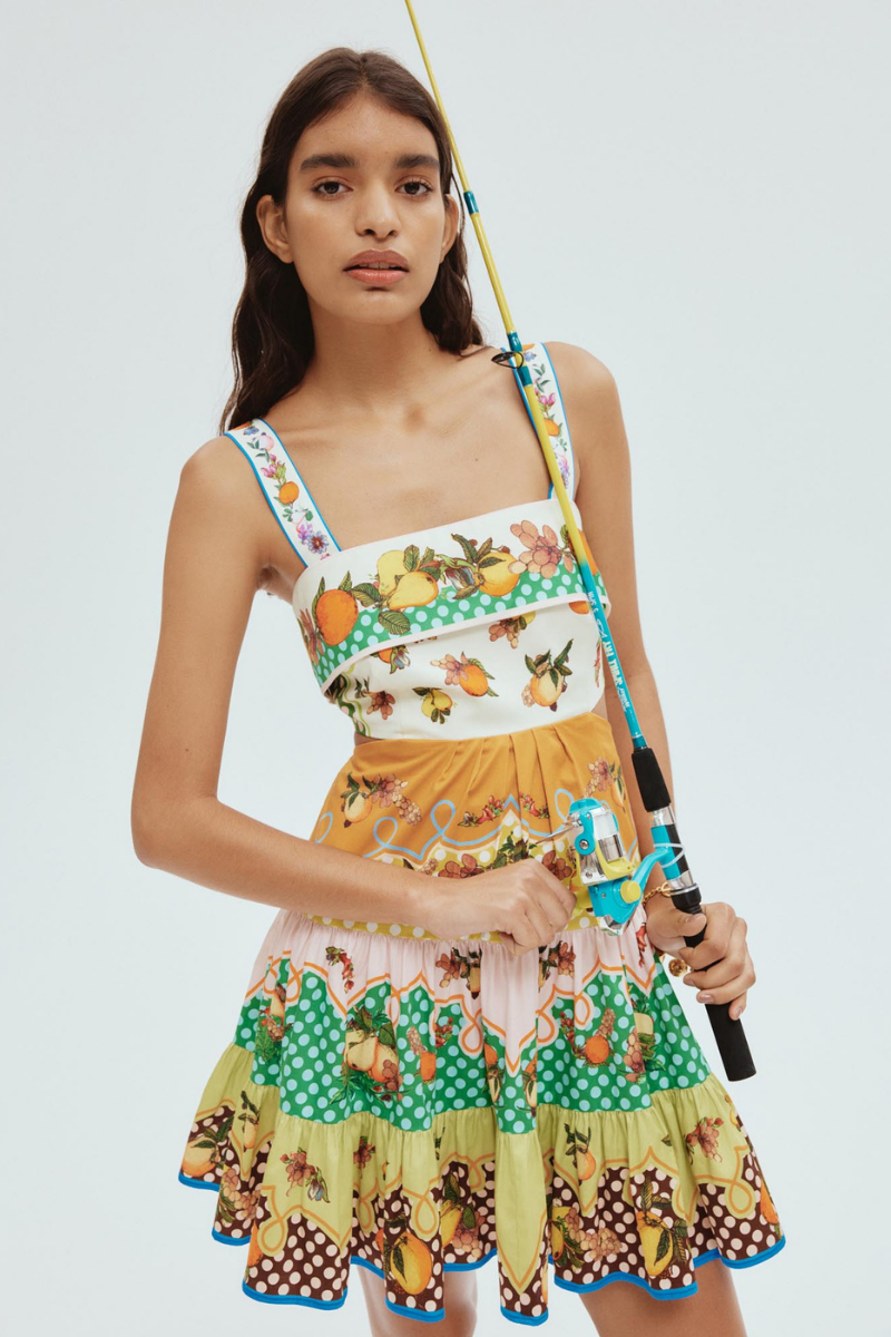 Woman in colorful citrus print mini dress holding fishing rod