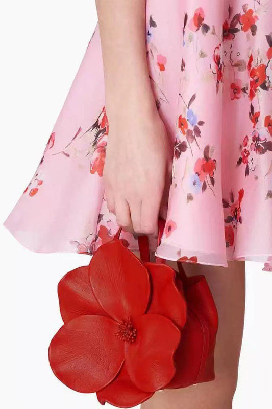 Close-up of a red leather bucket bag shaped like a flower held by a person wearing a floral dress.