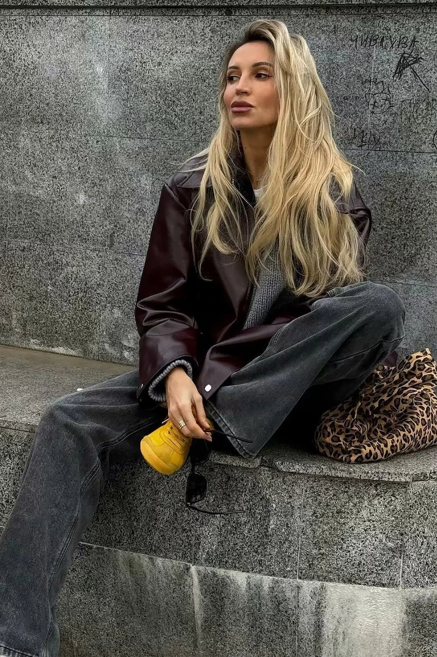 Woman in burgundy faux leather bomber jacket and black jeans.