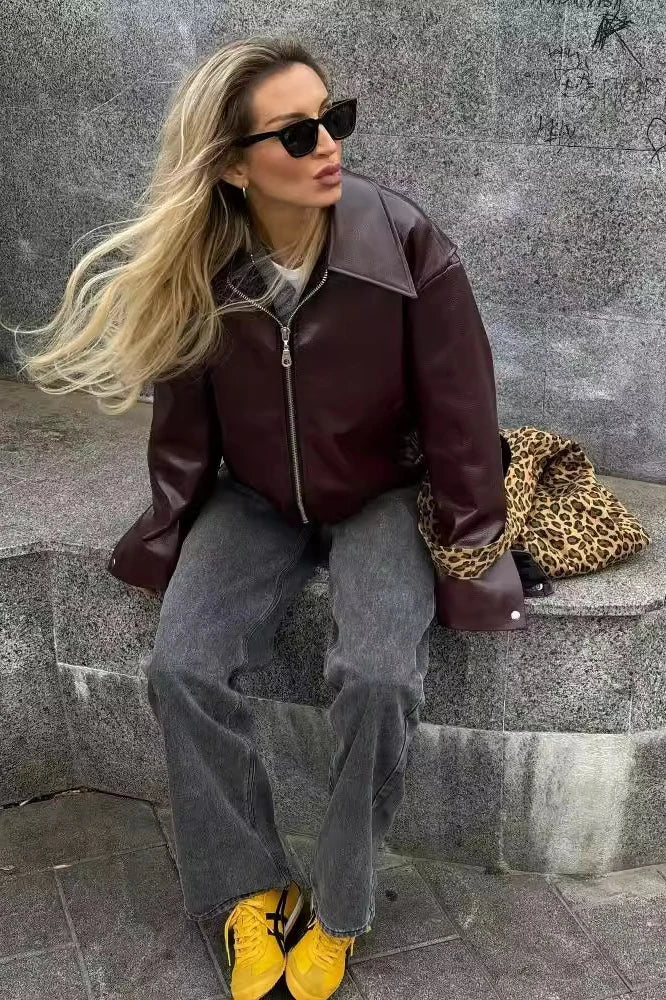 Woman in burgundy faux leather bomber jacket and black jeans.